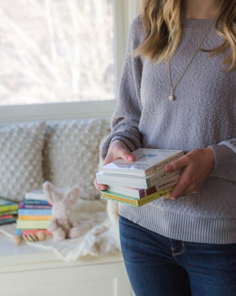 Woman in blue sweater holding stack of board books.