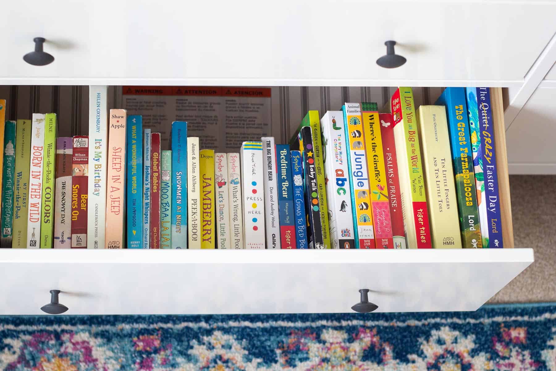 An open dresser drawer showcasing a row of colorful board books.