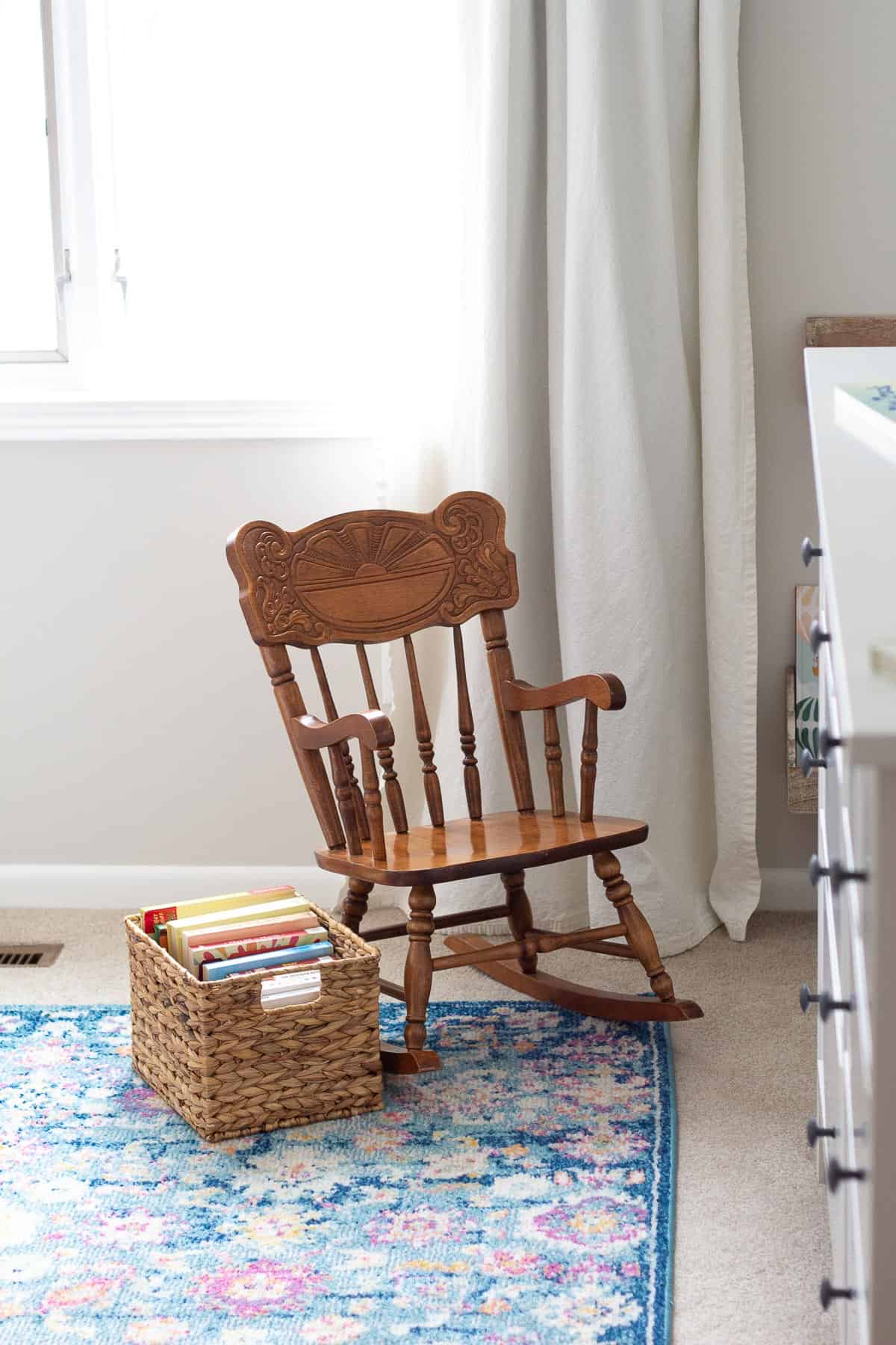 A small rocking chair with a basket of books alongside it.