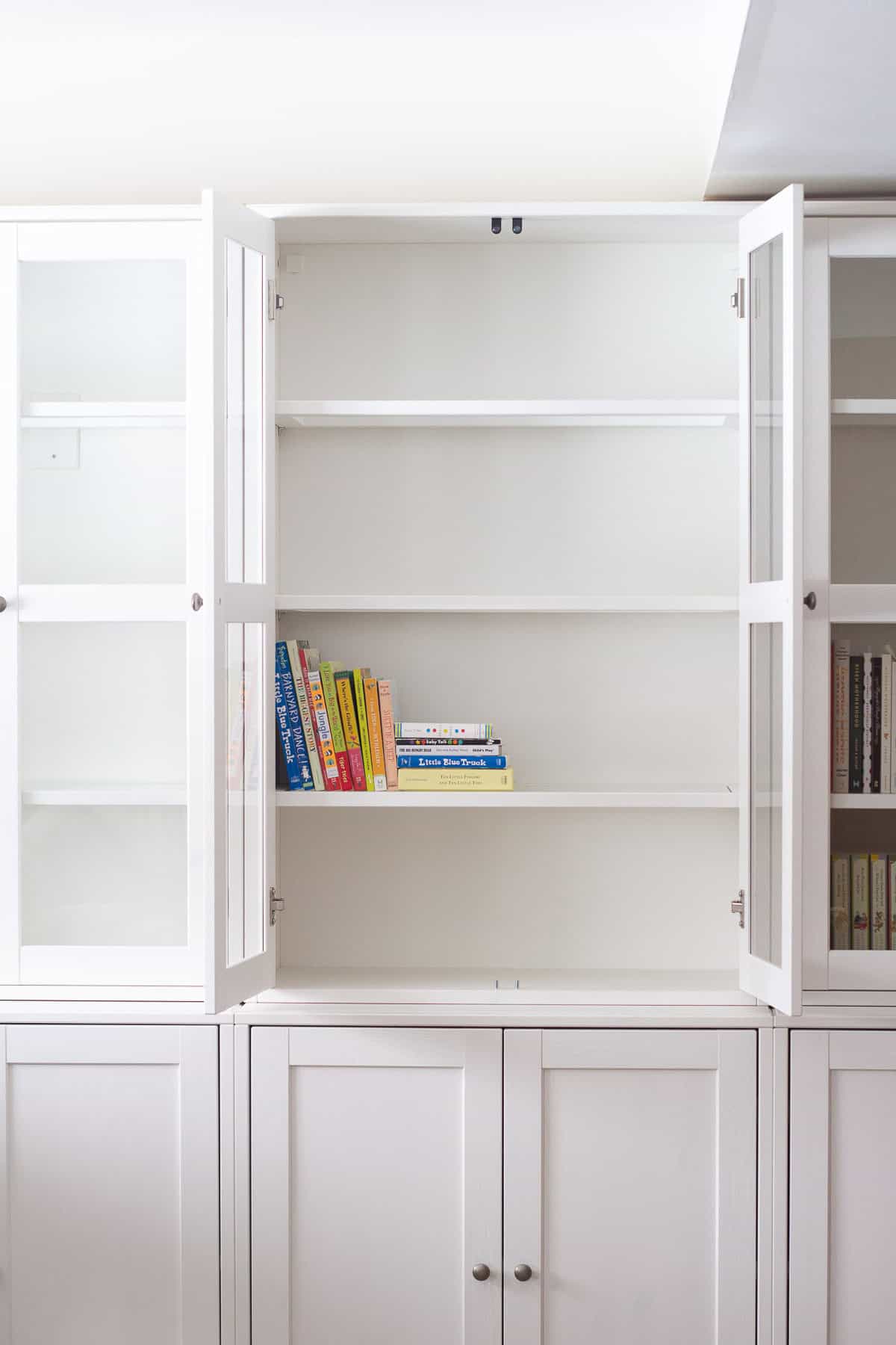 White built-in cabinets with colorful board books on the interior shelf.